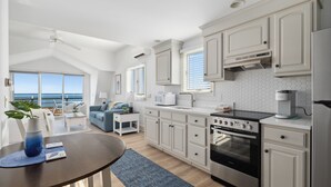 A modern kitchen with white cabinets, a built-in oven, and a view of the ocean through large windows. - Chatham Tides (South Chatham)