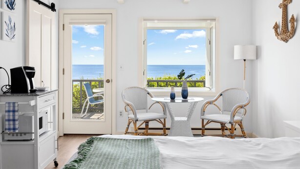 A room with a bed, two wicker chairs, a small table, a coffee maker, and a view of the sea through a window. - Chatham Tides (South Chatham)