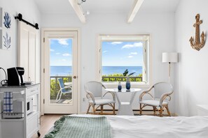 A room with a bed, two wicker chairs, a small table, a coffee maker, and a view of the sea through a window. - Chatham Tides (South Chatham)