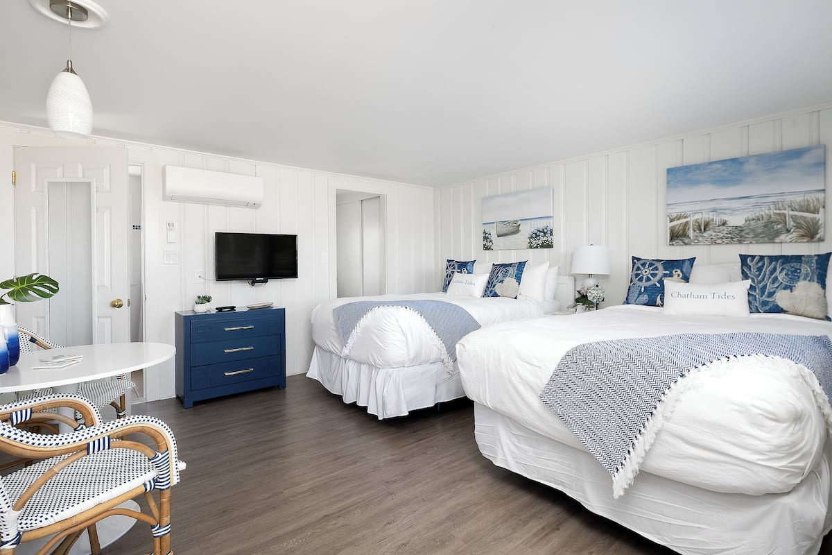 A hotel room with two beds, a TV, a desk, and a dining area with wicker chairs.