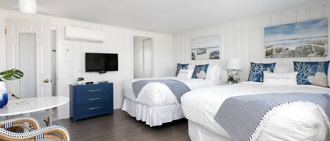 A hotel room with two beds, a TV, a desk, and a dining area with wicker chairs.