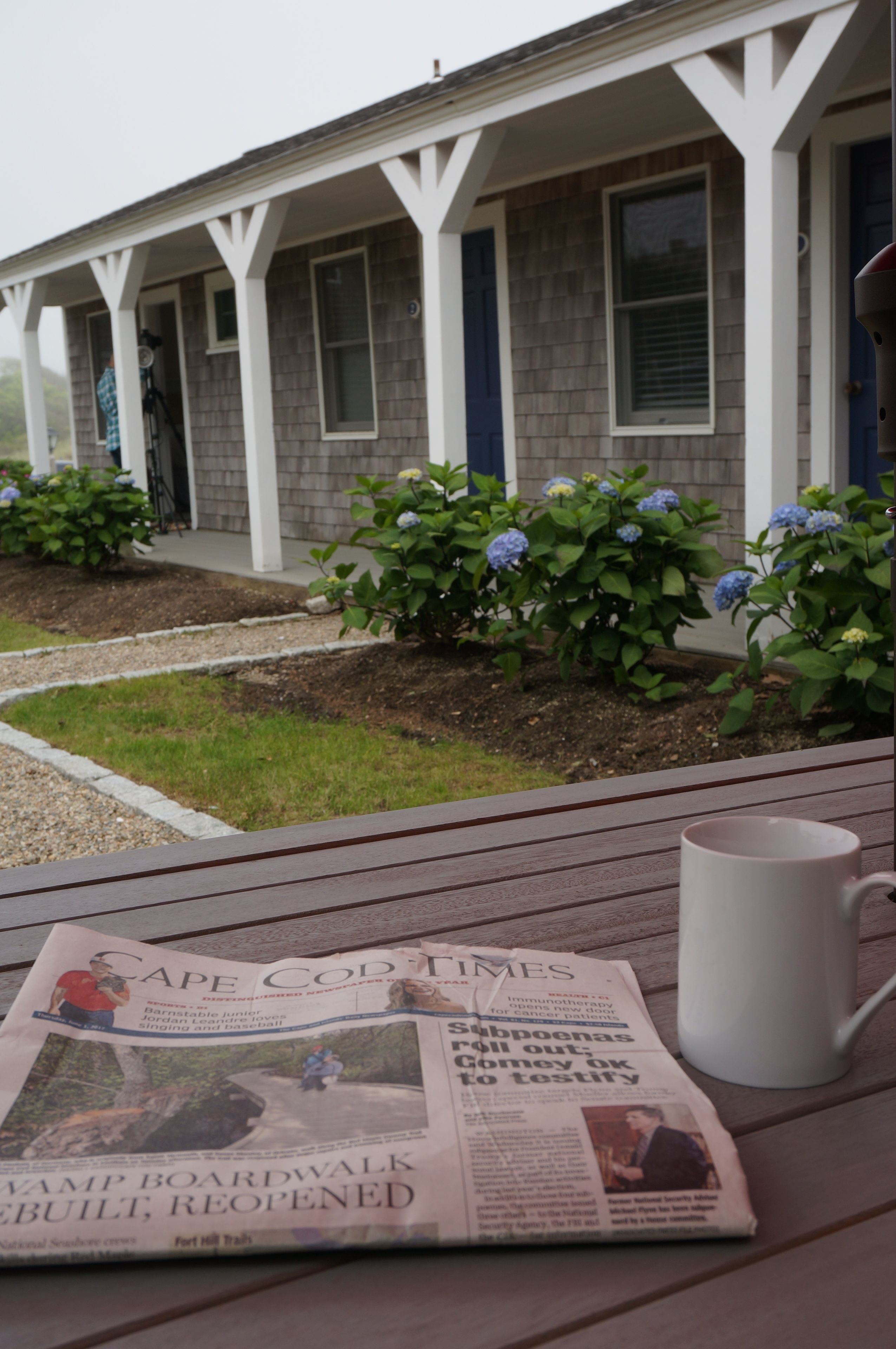 A Cape Cod Times newspaper on a wooden table with a white mug beside it.