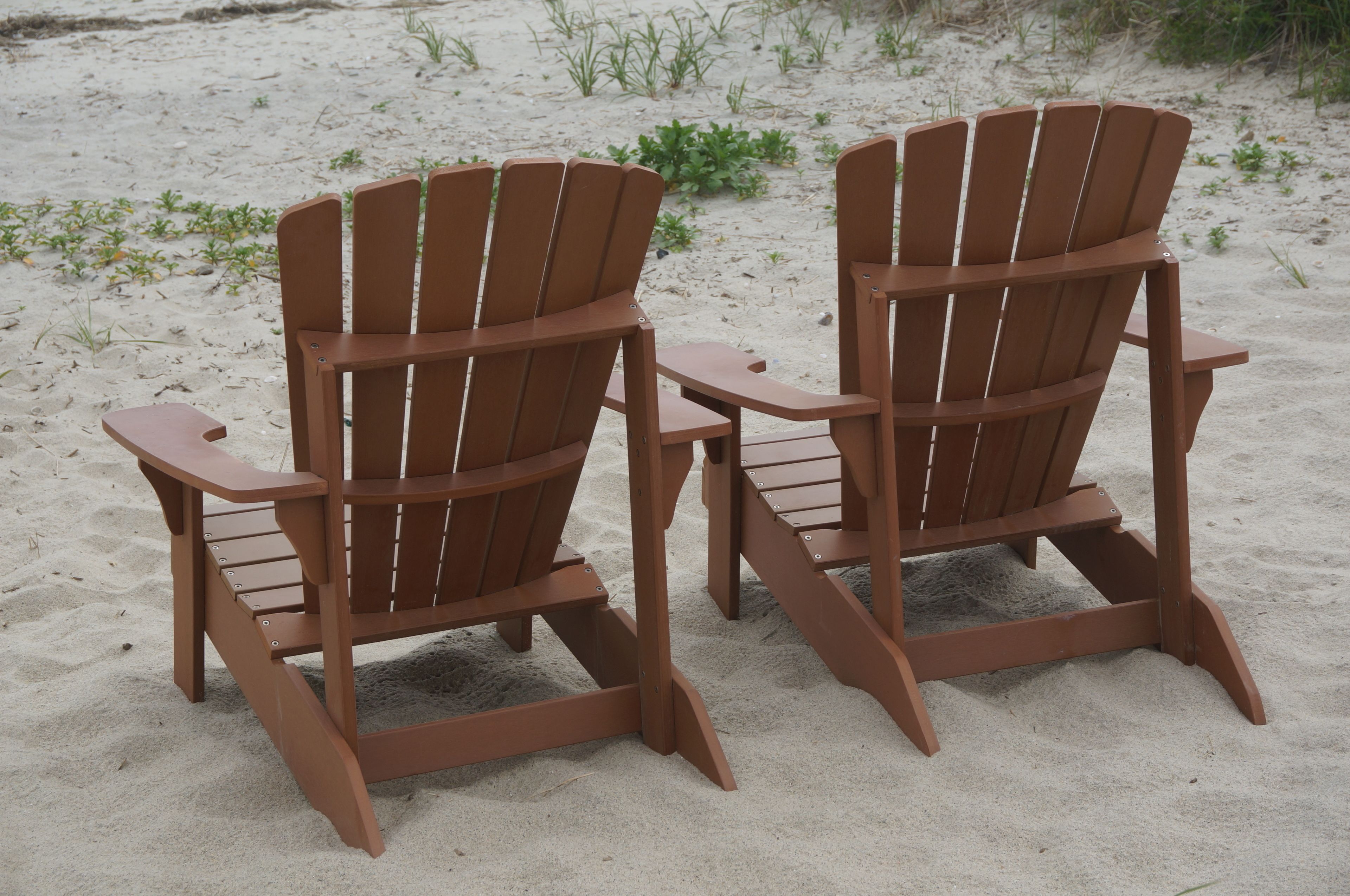 To træstole af Adirondack-typen på en sandstrand.