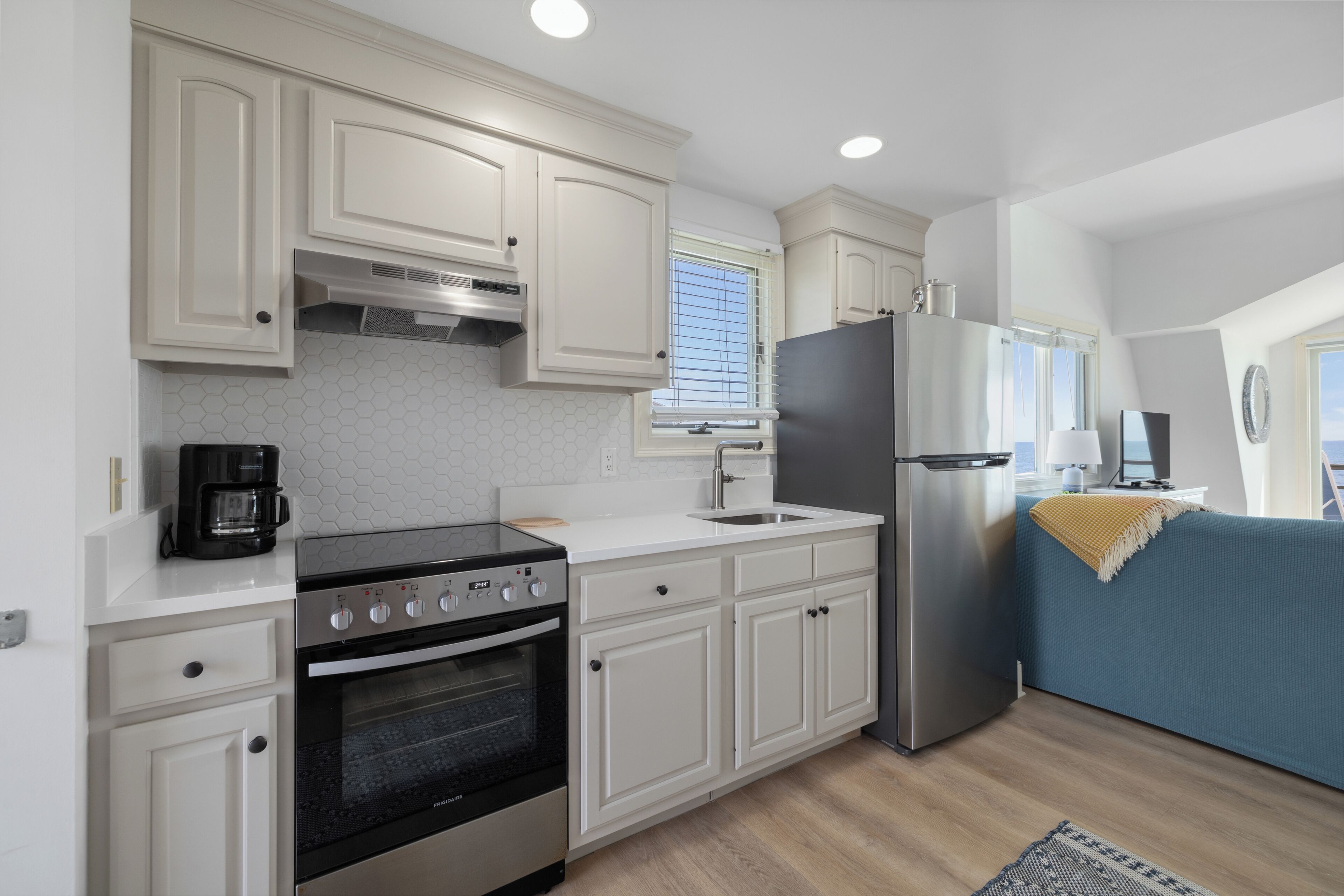 A modern kitchen with white cabinets, a stainless steel refrigerator, a built-in oven, and a coffee maker.