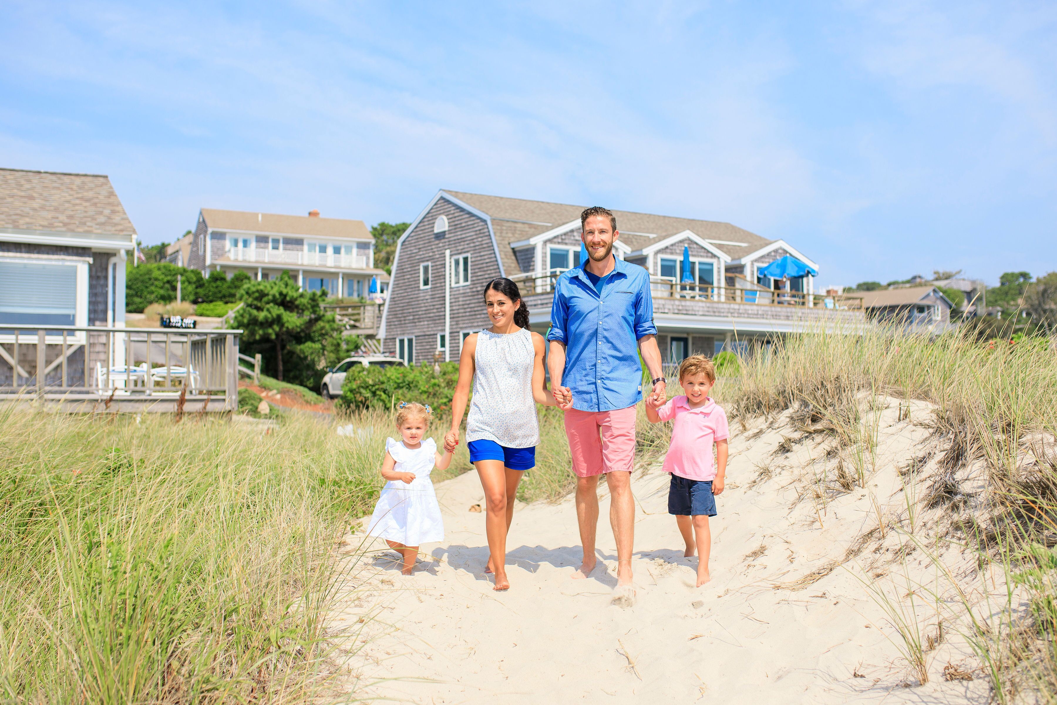 A family walking on a sandy path with beach houses in the background.