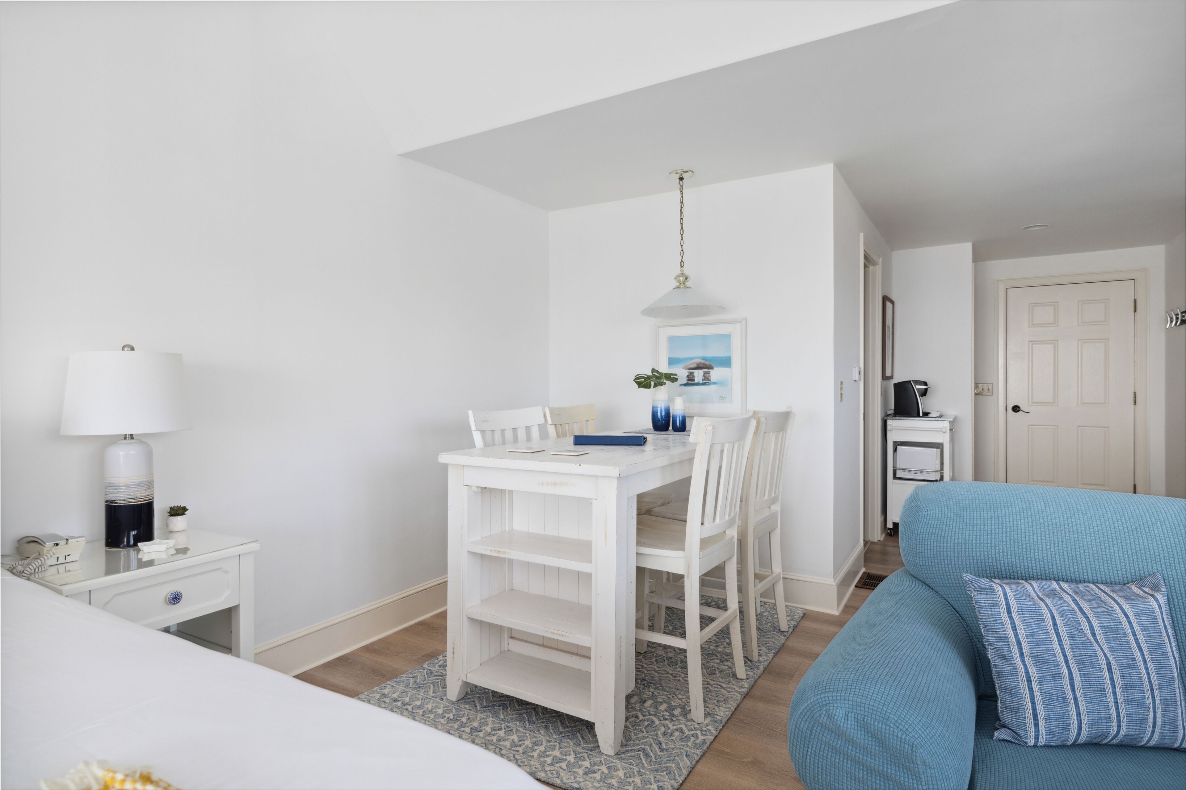 Una habitación compacta con un escritorio blanco, un sofá azul y una pequeña mesa de comedor.