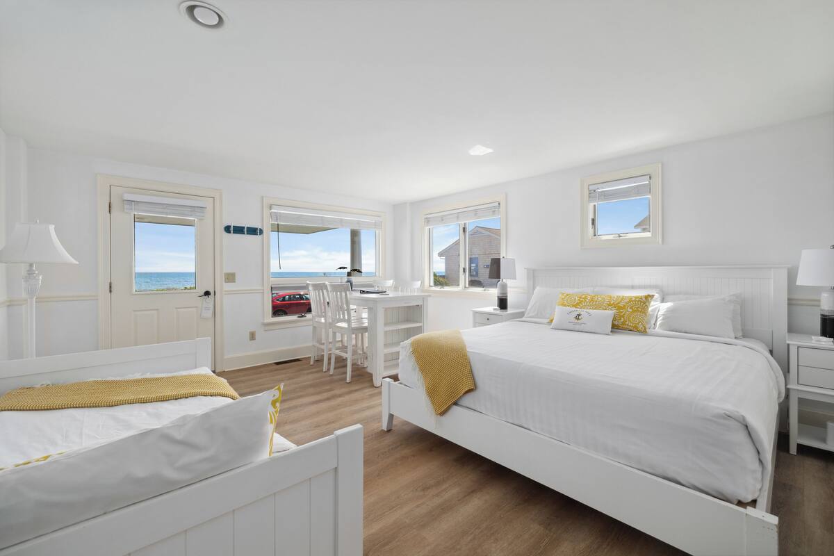 A hotel room with a bed, a desk, and a view of the sea.