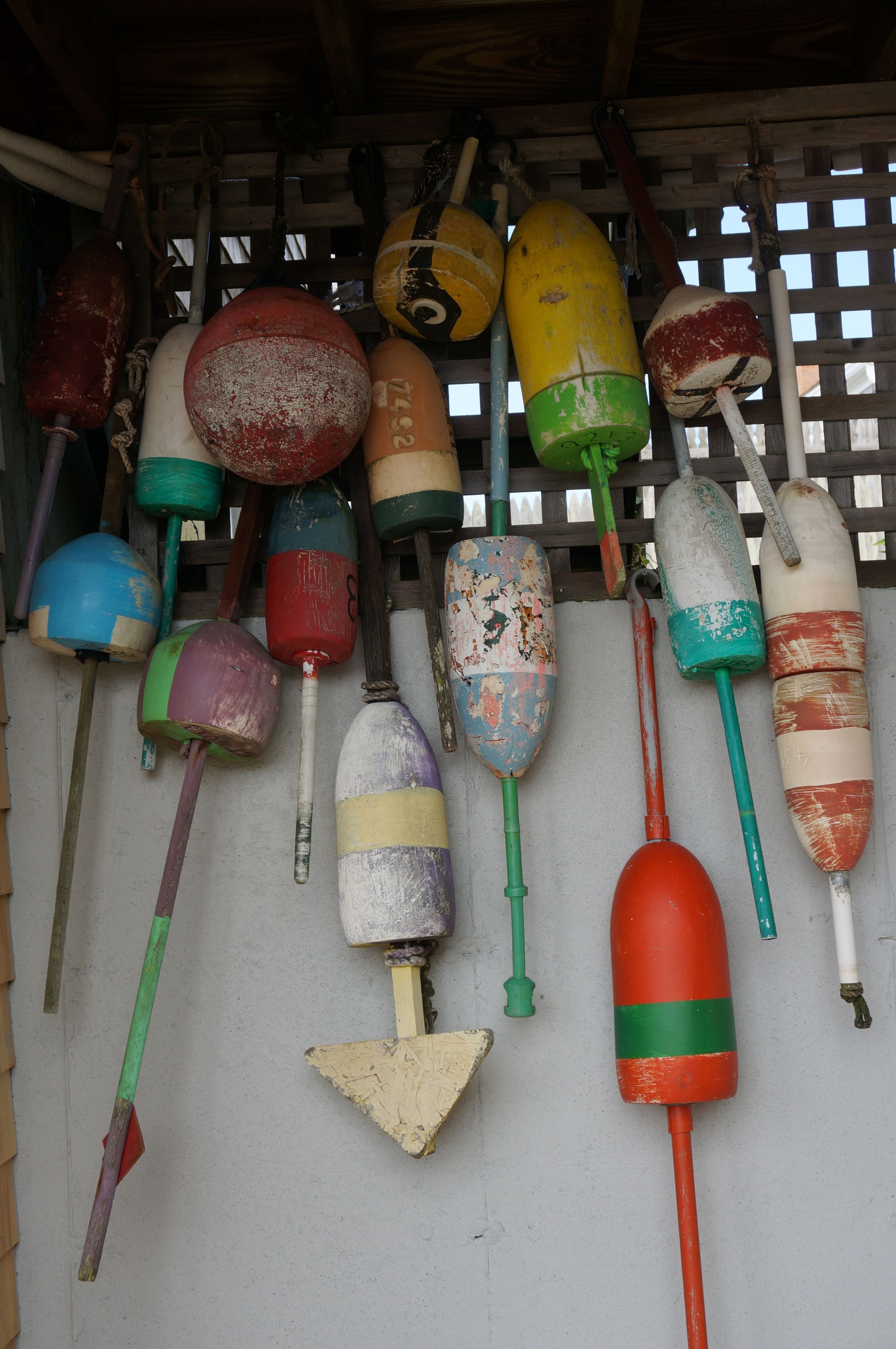 A collection of buoys hanging on a wooden lattice wall.