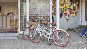 A white bicycle with brown tires parked outside a building with a wooden exterior. - Chatham Tides (South Chatham)