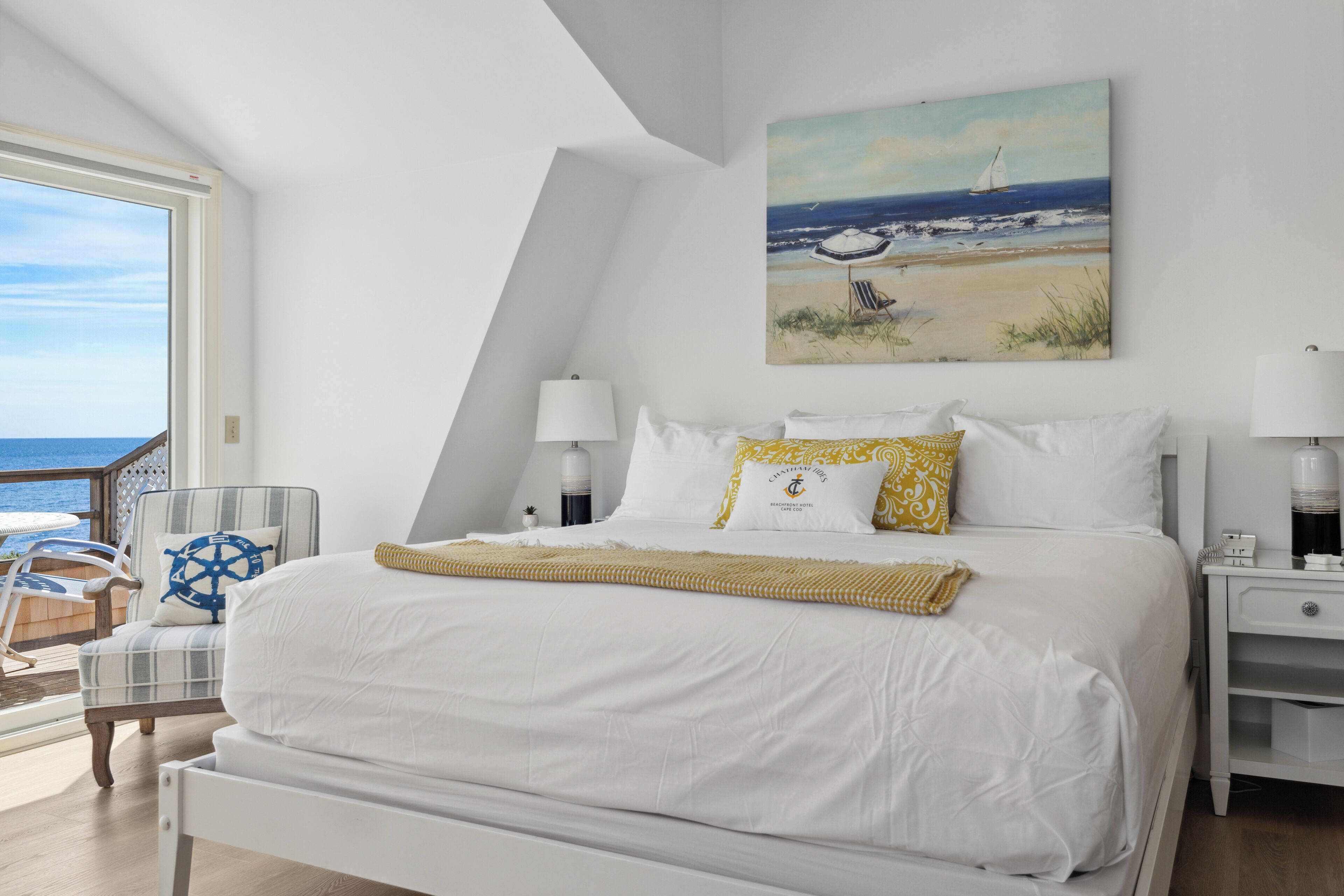 A bedroom with a large bed, a chair, a nightstand, and a painting of a beach scene.