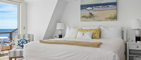 A bedroom with a large bed, a chair, a nightstand, and a painting of a beach scene.