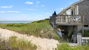 A beachfront property with a wooden deck, a sign labeled "SHOWER," and surfboards stored outside. - Chatham Tides (South Chatham)