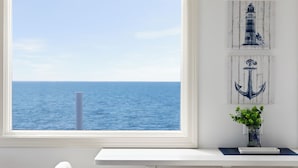 A room with a large window overlooking the sea, a white desk, and nautical-themed decor. - Chatham Tides (South Chatham)