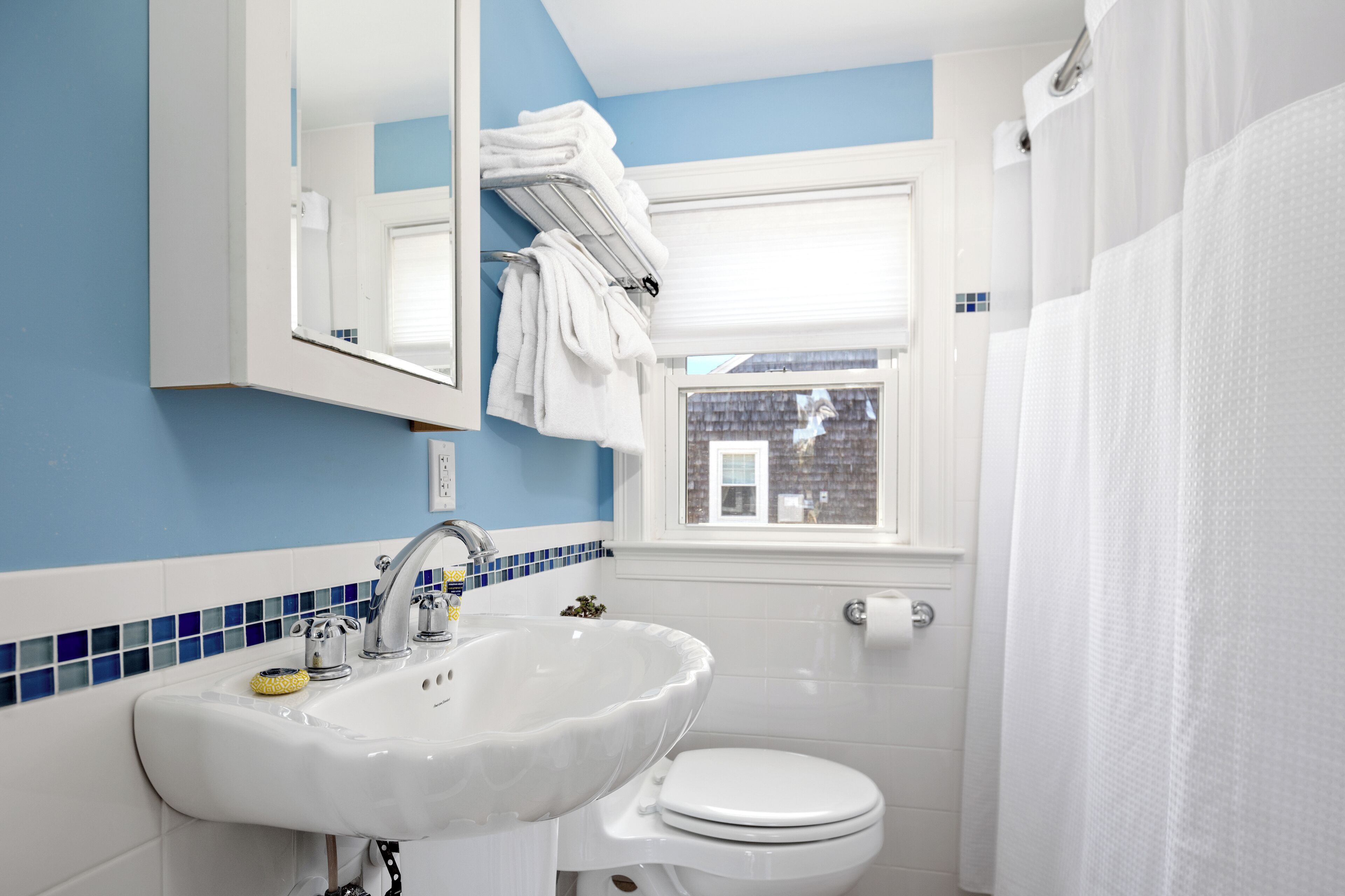 Une salle de bain avec un lavabo blanc, des toilettes et une fenêtre donnant sur un bâtiment à l’extérieur.
