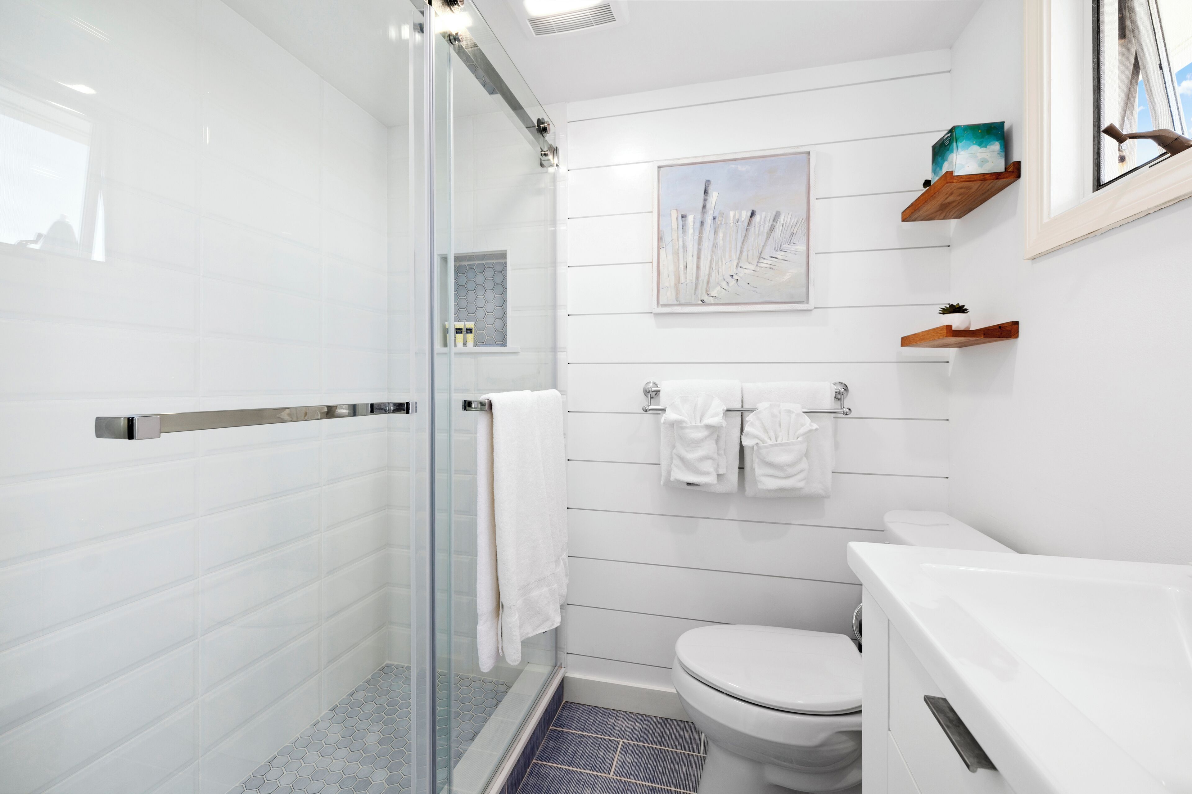 Ein modernes Badezimmer mit Duschkabine aus Glas, weiß gefliesten Wänden, einer weißen Toilette und einem aufgehängten Bild.