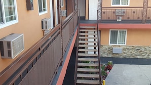 A multi-story building with a central staircase, air conditioning units, and a small garden area.