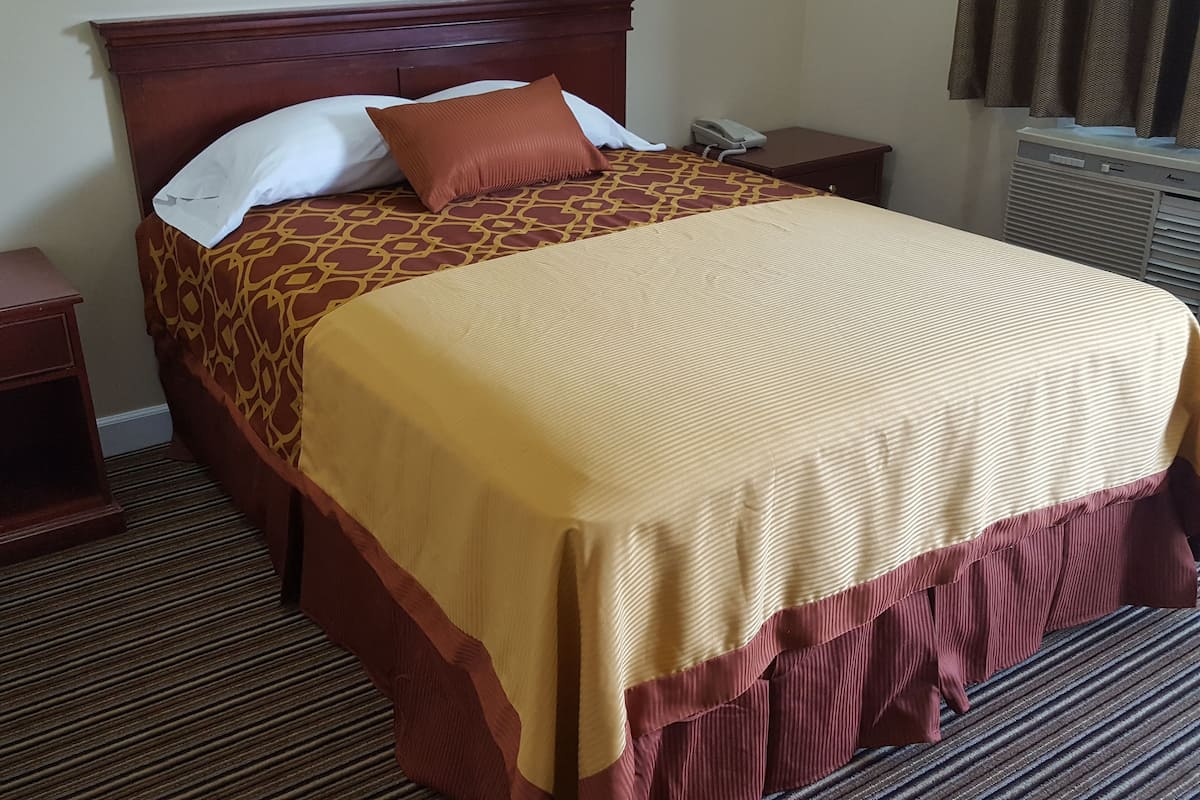 A neatly made bed with a patterned bedspread and pillows, a bedside table with a telephone, and a radiator in the room.