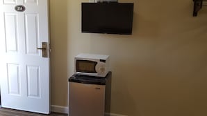 A room with a white door, a microwave on a stand, and a flat-screen TV mounted on the wall.
