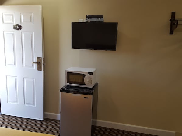 A room with a white door, a microwave on a stand, and a flat-screen TV mounted on the wall.