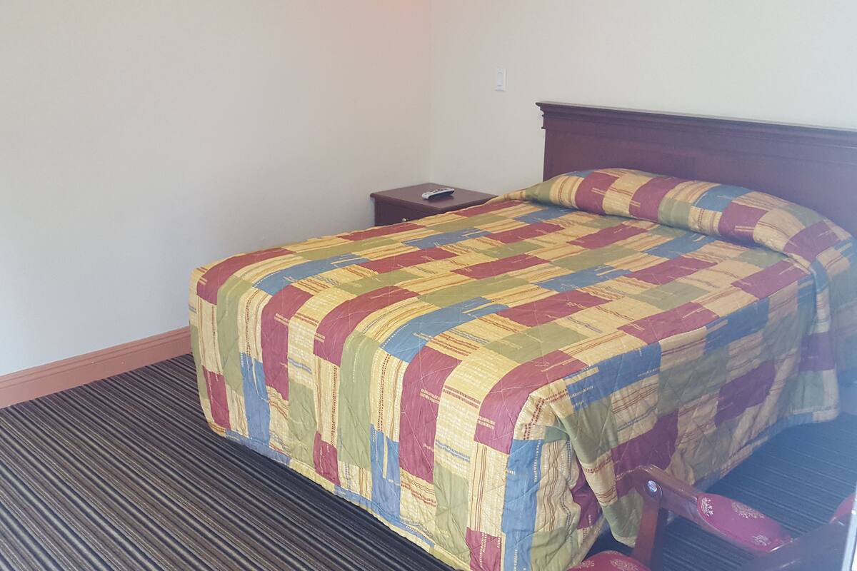 A hotel room with a bed, a nightstand, and a wall-mounted light fixture.