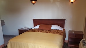 A hotel room with a large bed, a wooden headboard, two bedside tables with lamps, and a telephone.