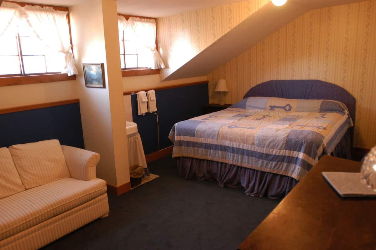 A bedroom with a bed, a sofa, a window with curtains, a bedside table, and a lamp.