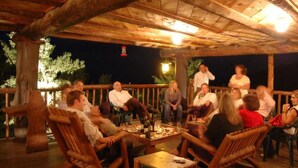 A group of people seated on wooden chairs and tables under a wooden roofed area, likely a patio or deck, with a view of trees in the background. - Baldpate Inn (Estes Park)