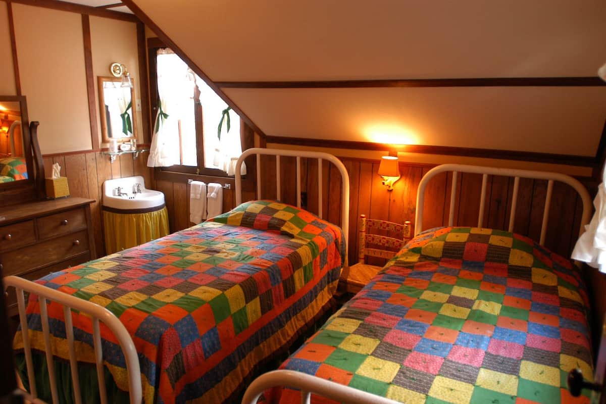 A bedroom with two single beds, a wooden dresser, a sink, and a window with curtains.