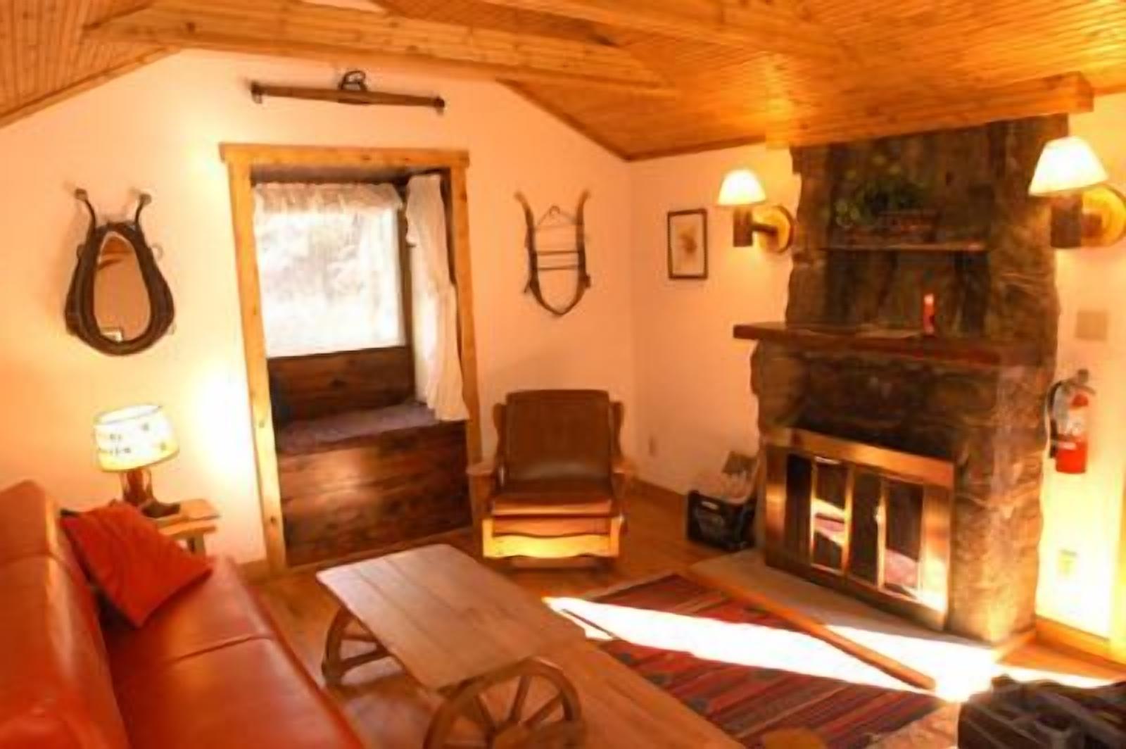 A cozy room with a stone fireplace, wooden furniture, and a window with curtains.