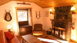 A cozy room with a stone fireplace, wooden furniture, and a window with curtains. - Baldpate Inn (Estes Park)