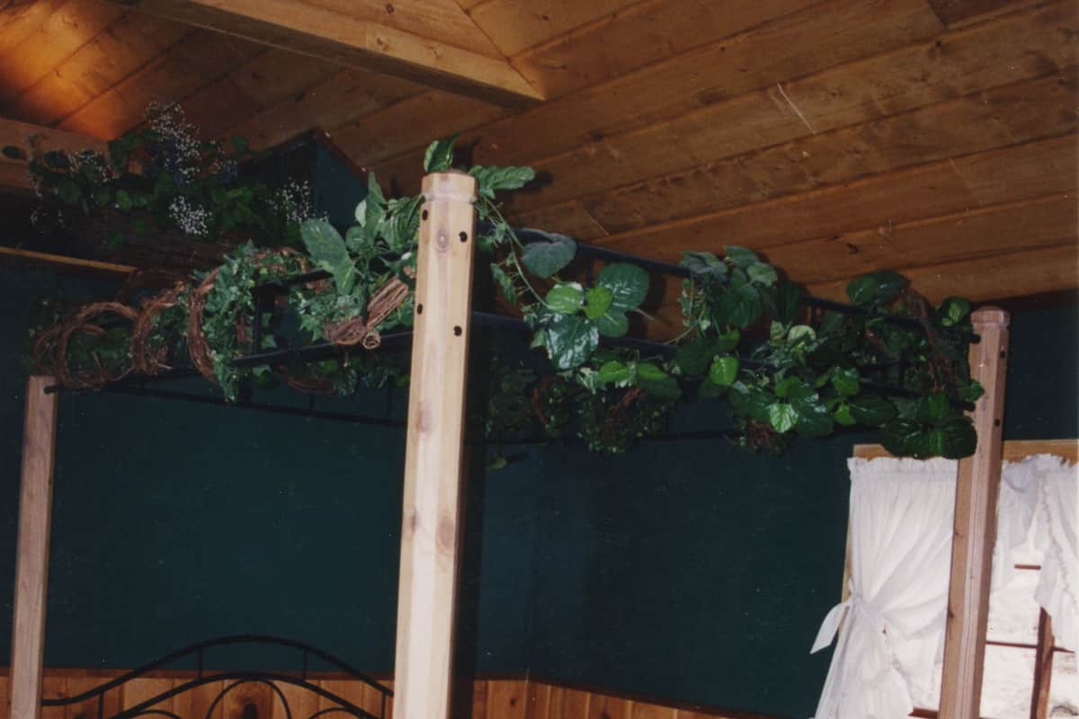 A wooden-framed bed with a mattress and pillows, surrounded by a wooden wall and a green plant overhead.