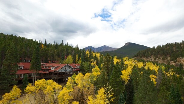 A lodge with a red roof and multiple buildings, surrounded by dense forest and mountains.