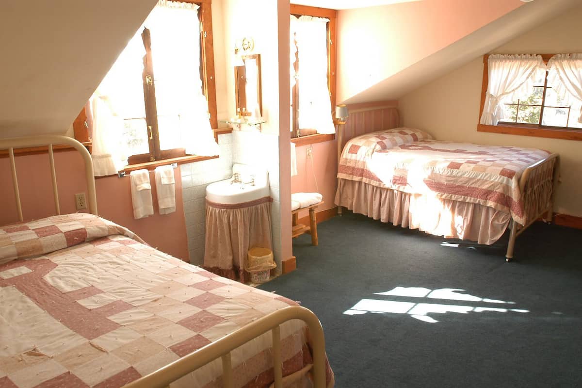 A dormitory room with two beds, a sink, and a window.