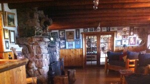 A cozy interior with wooden flooring, a stone fireplace, and a bar area with framed pictures. - Baldpate Inn (Estes Park)