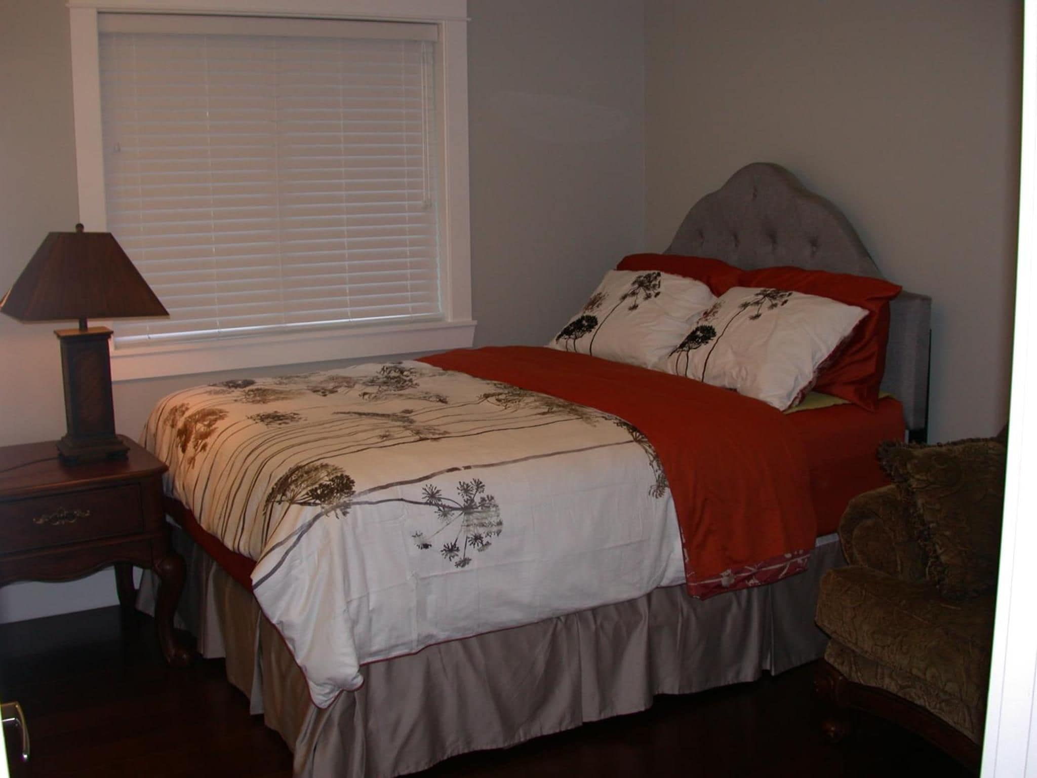 A bedroom with a bed, a nightstand, a lamp, and a window with blinds.