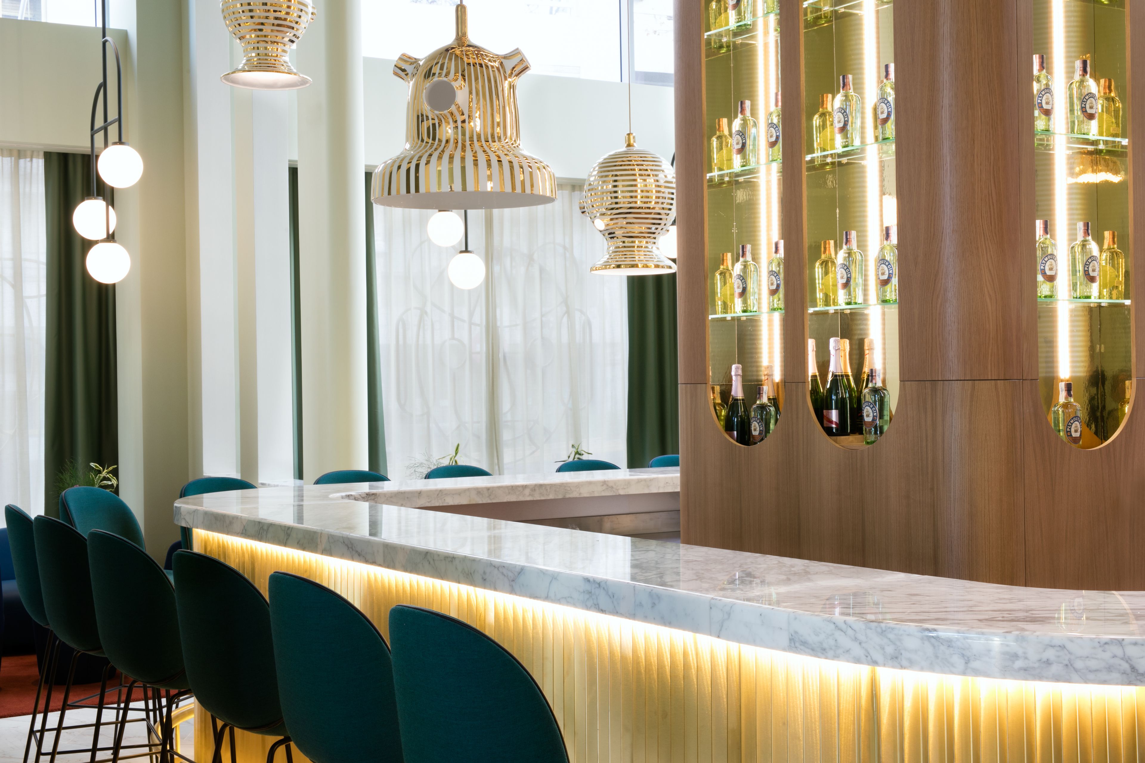 A bar area with a curved marble countertop, teal chairs, and hanging wicker light fixtures.