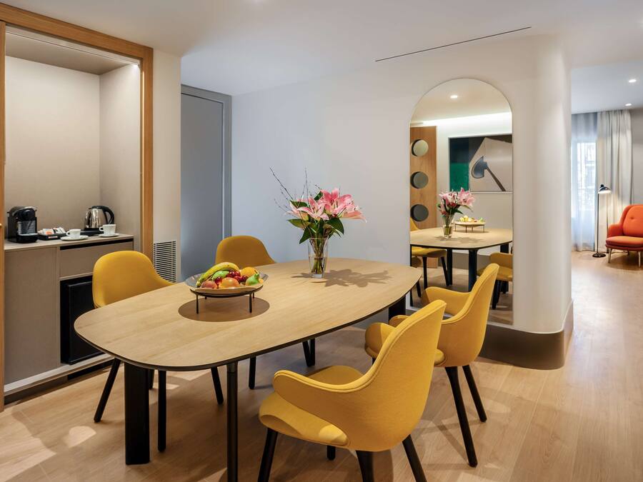 A modern dining area with a wooden table, yellow chairs, and a vase of flowers.