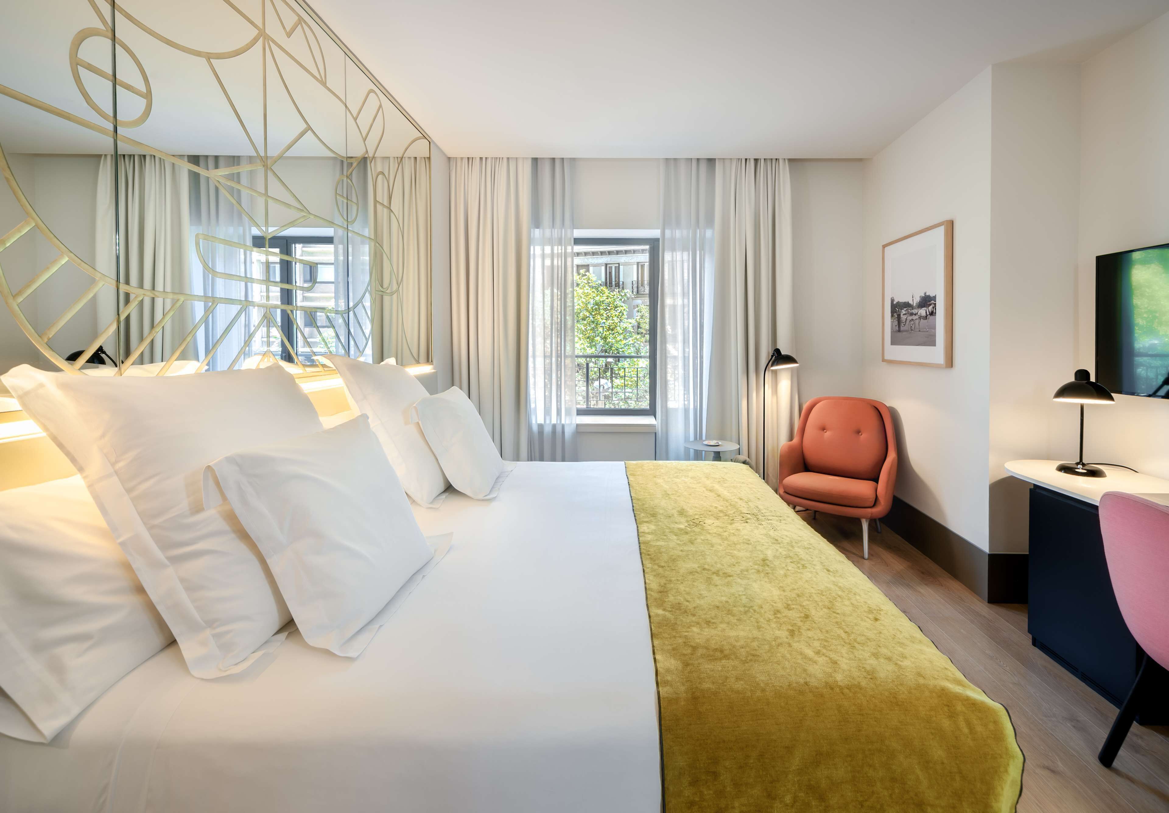 A hotel room with a large bed, a desk with a chair, a television, and a window with curtains.
