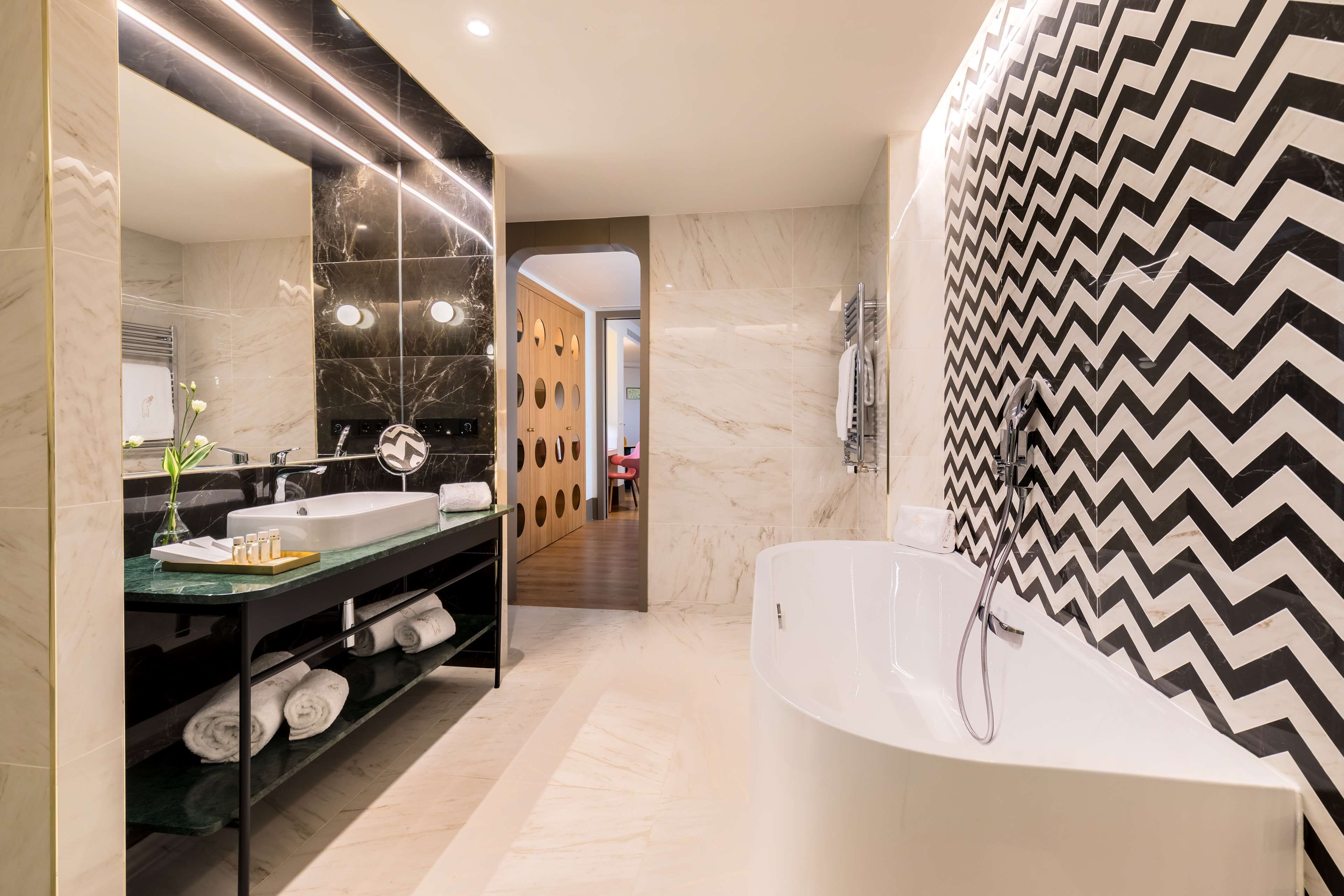 Ein modernes Badezimmer mit großem Spiegel, einer weißen Badewanne und einem Waschtisch mit Waschbecken und Handtuchhalter.
