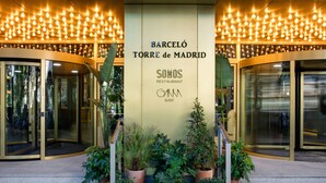 The entrance of Barceló Torre de Madrid with glass doors, potted plants, and a sign for SOMOS restaurant and GAMA bar. - Barceló Torre de Madrid (Madrid)