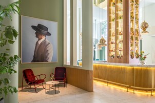 A lobby with a large framed portrait, red chairs, a reception desk with a wine display, and a large window.