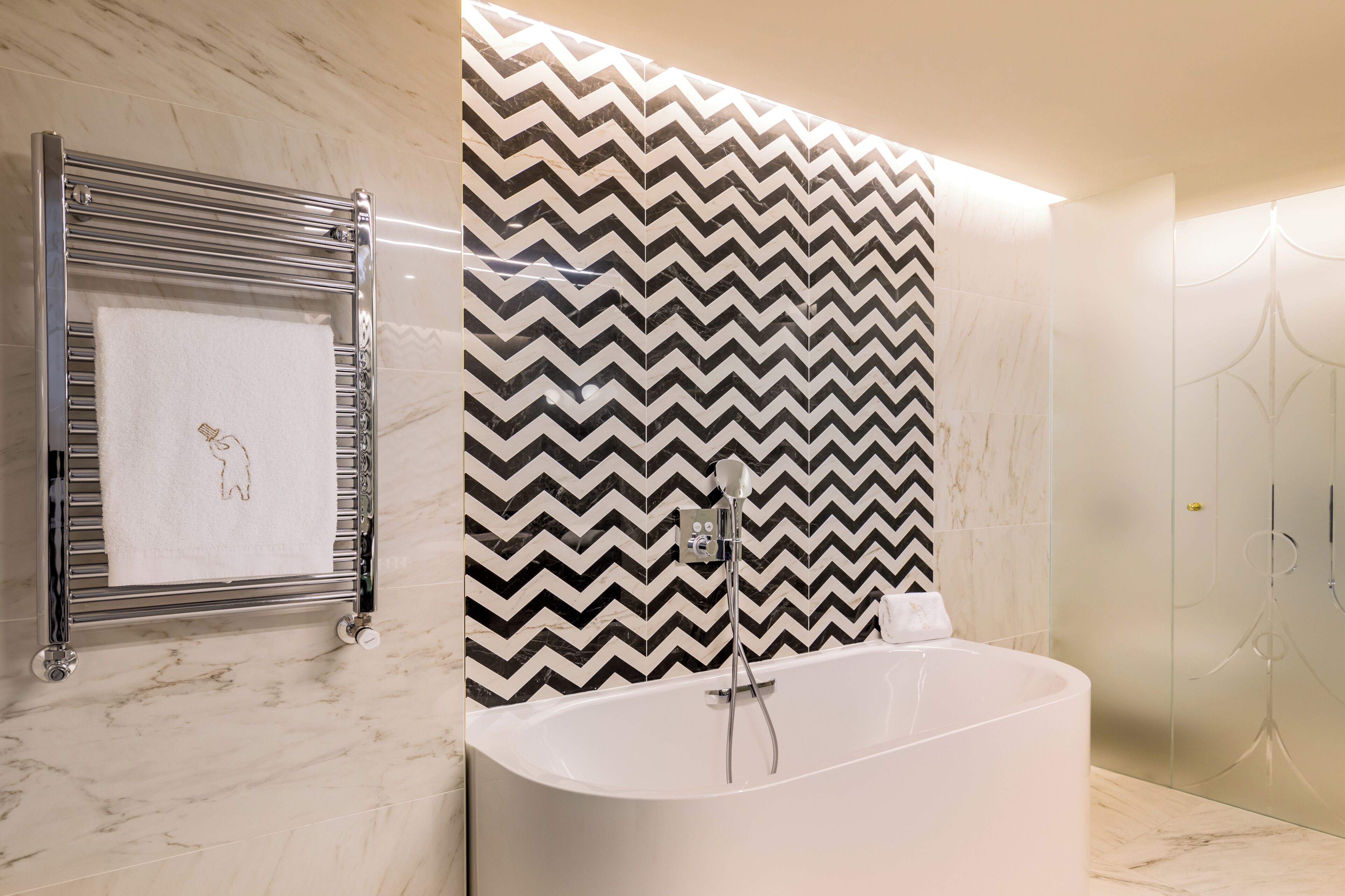 Un baño moderno con una bañera independiente, un perchero con una toalla y un espejo.