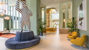 A spacious lobby with a modern blue sofa, yellow armchairs, and a unique striped sculpture. - Barceló Torre de Madrid (Madrid)