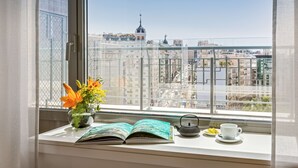A window with a view of a cityscape, a potted plant with flowers, an open book, a teapot, and a cup on a windowsill. - Barceló Torre de Madrid (Madrid)