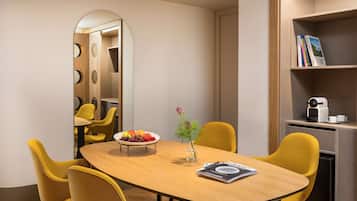 Una sala de conferencias moderna con una mesa de madera, sillas amarillas, un frutero, un florero y una estantería con libros y una máquina de café.