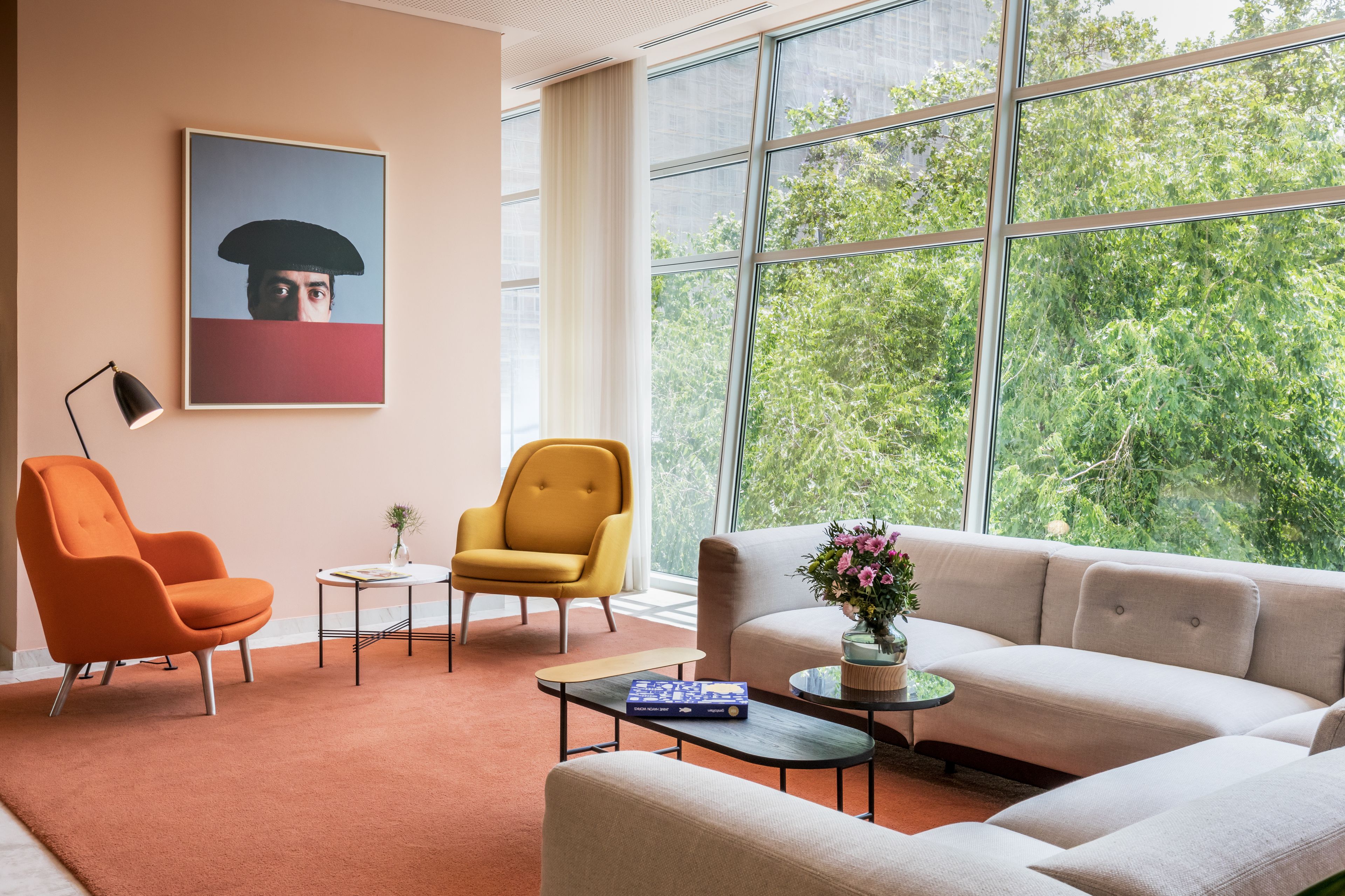 Ein modernes Wohnzimmer mit großem Fenster, einer Couch, einem orangefarbenen Sessel, einem gelben Sessel und einem Couchtisch.
