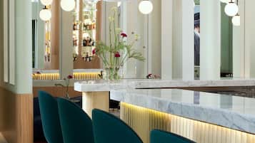 Una zona de bar con mostrador de mármol, taburetes de color turquesa y lámparas colgantes.