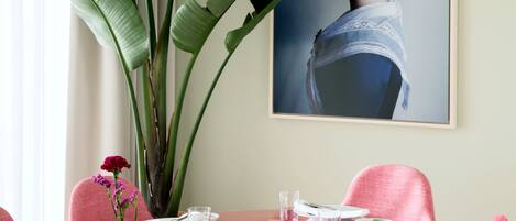 A dining area with a glass table set for four, surrounded by pink chairs.