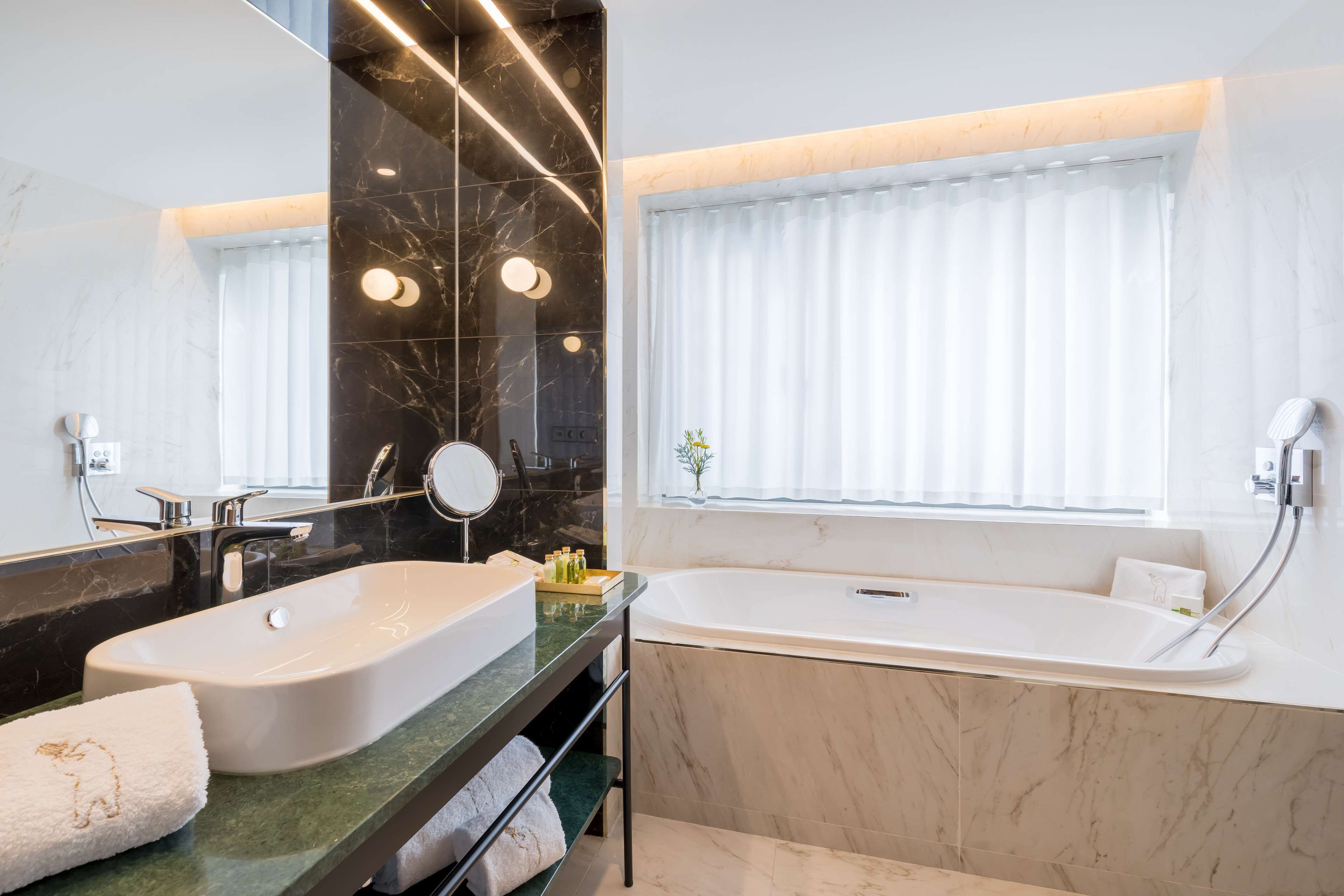 A modern bathroom with dual sinks, a large mirror, and a standalone bathtub.