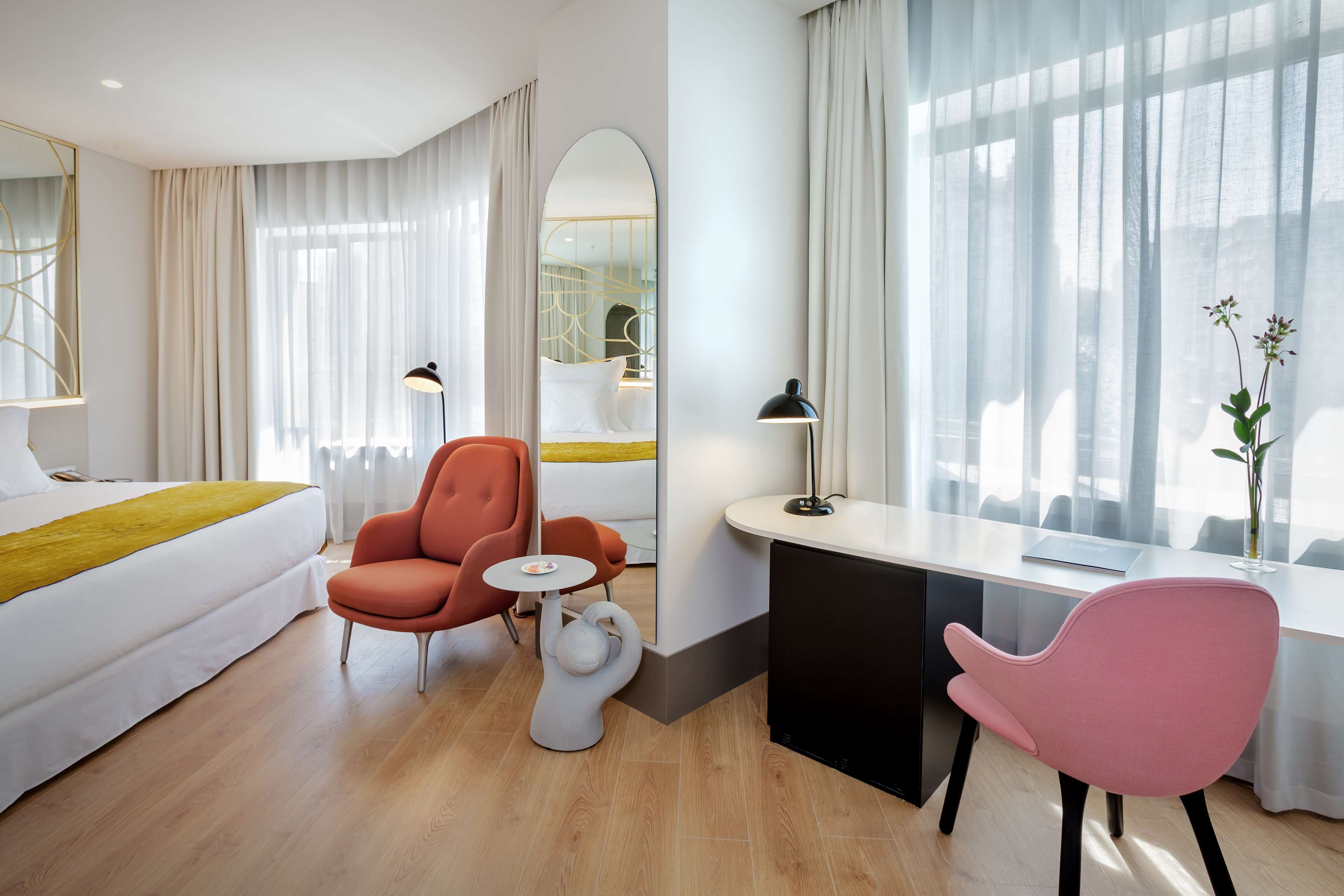 Una habitación de hotel moderna con una cama, dos sillas, un escritorio y un ventanal con cortinas.